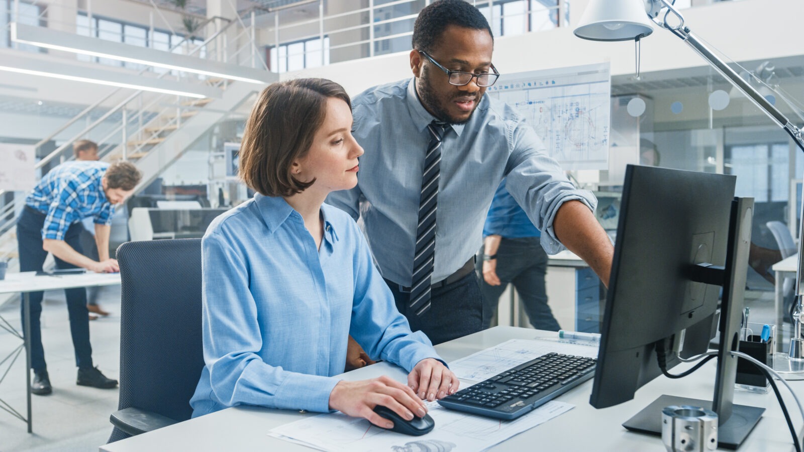 Man in a tie collaborating with a woman in front of a computer